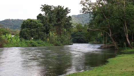 4k-Schöne-Weitwinkelaufnahme-Eines-Flusses-Mit-Seilschaukel,-Die-An-Einem-Baum-In-Thailand-Hängt