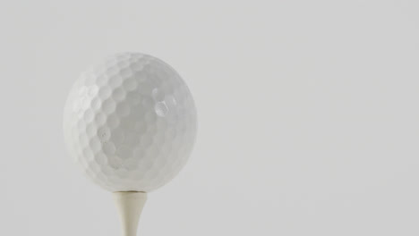 close up of golf tee and ball on white background, copy space, slow motion