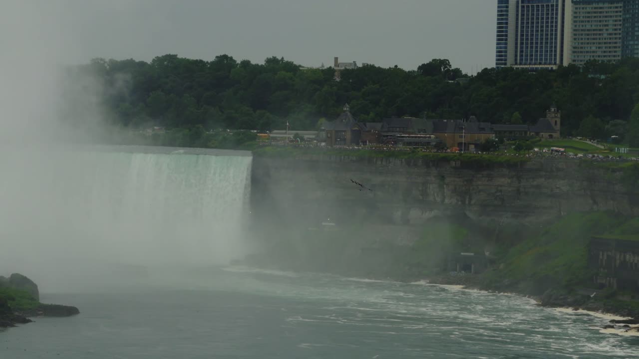 A misty view of Horseshoe Falls as city buildings and tourist facilities line the edge of the Canadian side of Niagara Falls