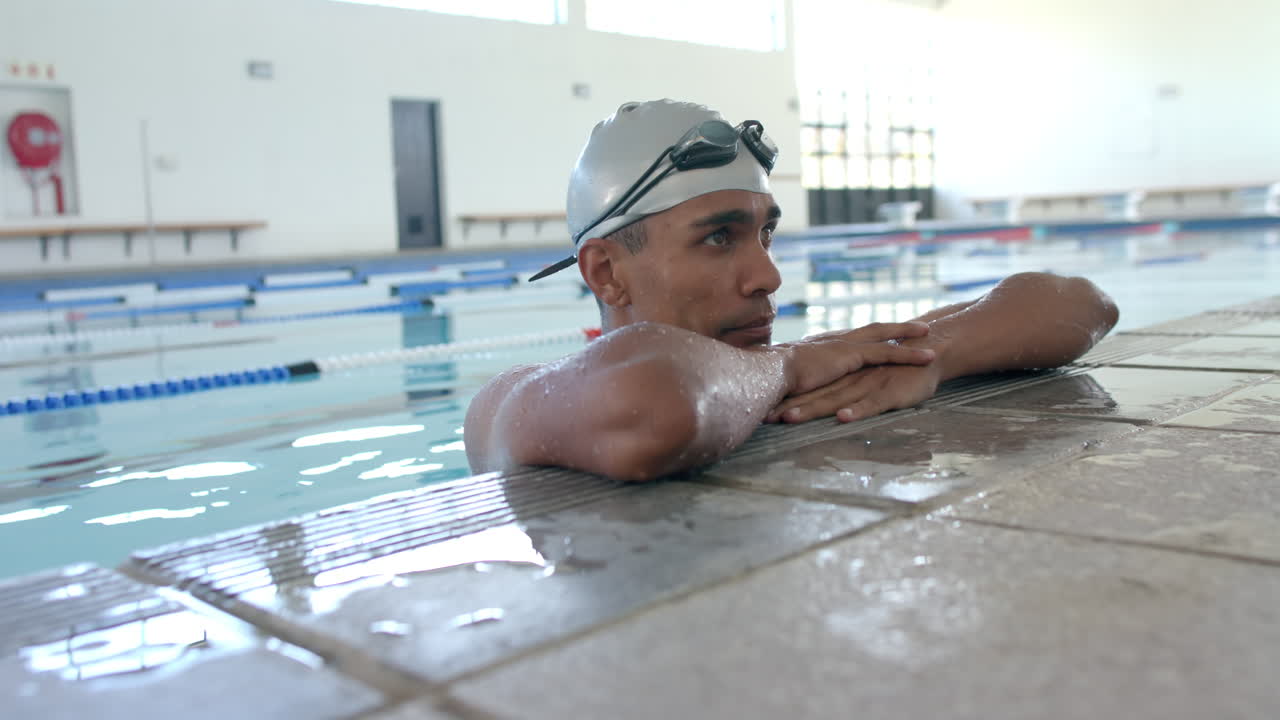 Young biracial male athlete swimmer rests at the pool edge