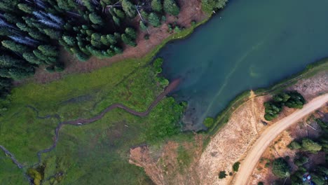 Beautiful-aerial-drone-top-bird's-eye-spinning-shot-of-a-small-stream-surrounded-by-a-field-of-grass-that-leads-into-the-Anderson-Meadow-Reservoir-lake-up-Beaver-Canyon-in-Utah-on-a-warm-summer-day