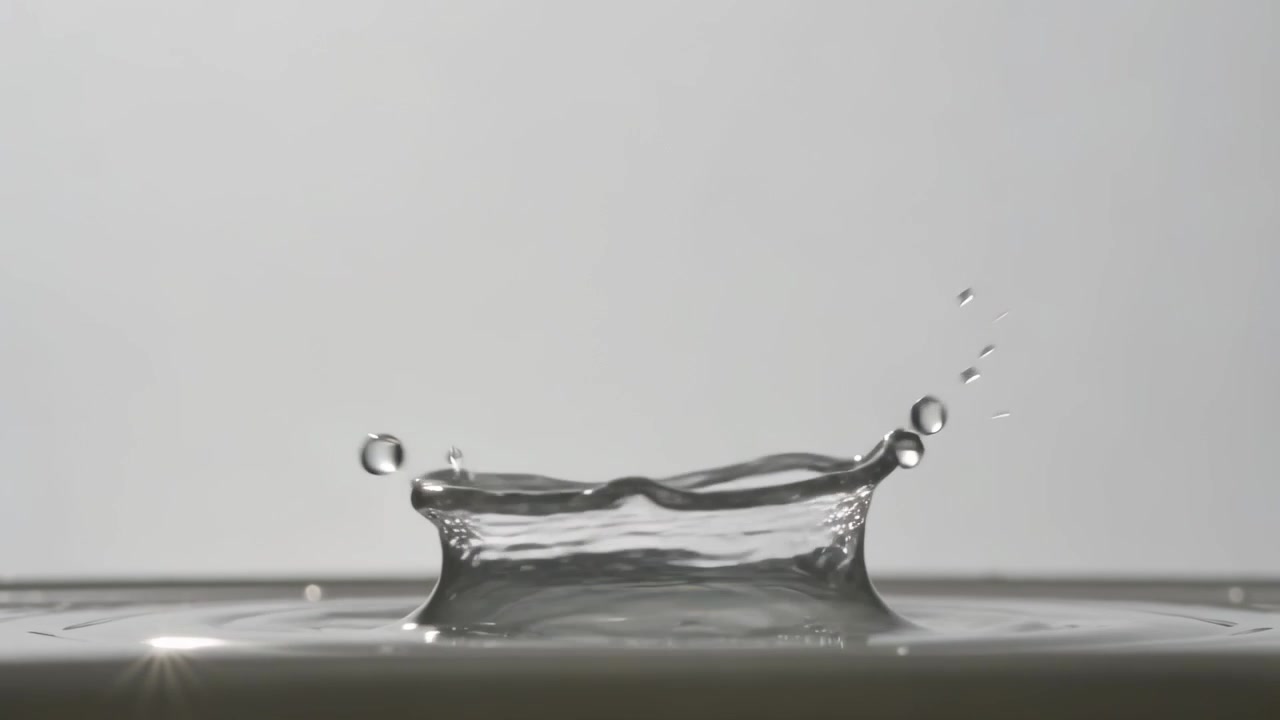 Falling clear droplet, gravity pulling down, forming crown, ejecting satellite droplets in studio