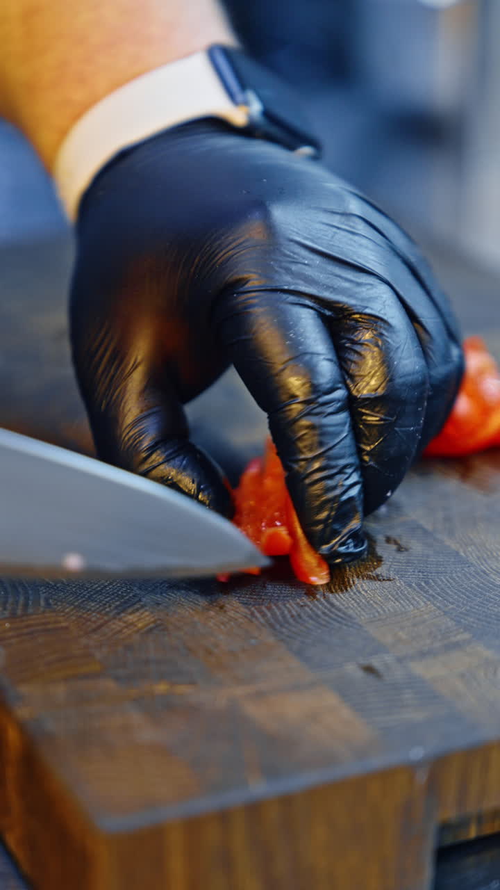 Male cook wearing black gloves cutting red pepper with a big knife. Salad preparation close up. Close up. Vertical video.