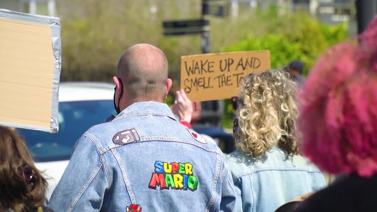 Middle close up to a group of protestants looking behind wearing super mario denim jacket with park environment in the backround slow motion