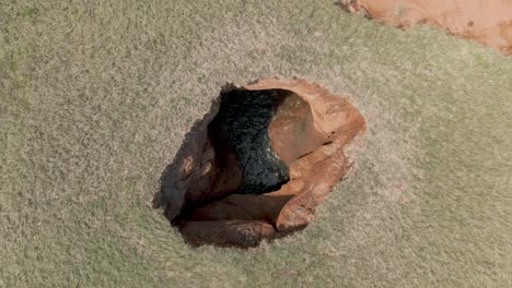 Toma-De-Arriba-Hacia-Abajo-De-Un-Agujero-Con-Agua-En-El-Paisaje-Costero-De-Las-Islas-Magdalen,-Norte-De-Quebec,-Canadá---Drone-Aéreo