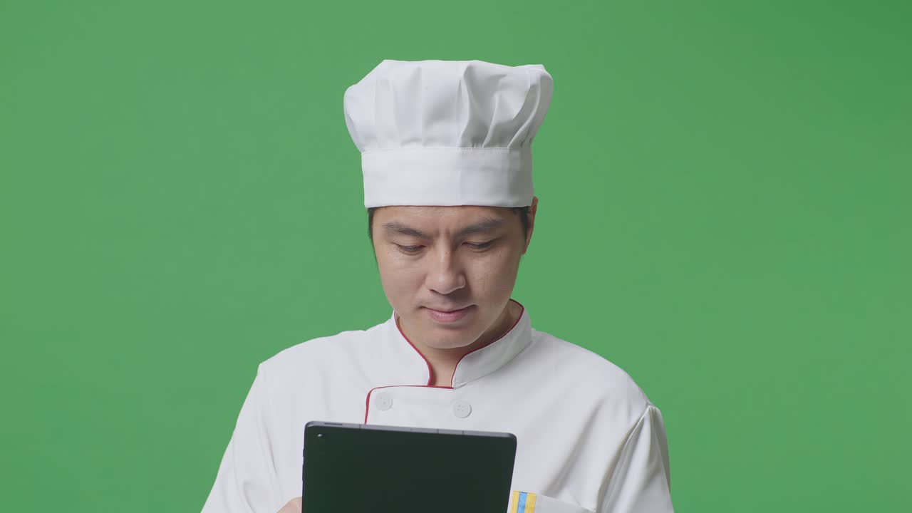 Close Up Of Asian Man Chef Using A Tablet While Standing In The Green Screen Background Studio