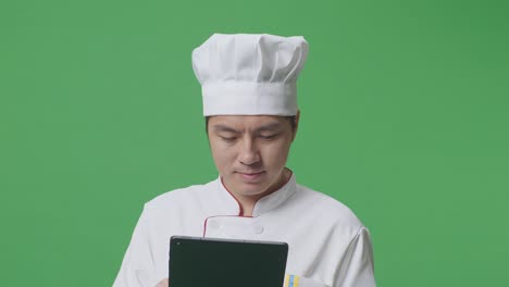 close up de un chef asiático usando una tableta mientras está de pie en el estudio de fondo de la pantalla verde