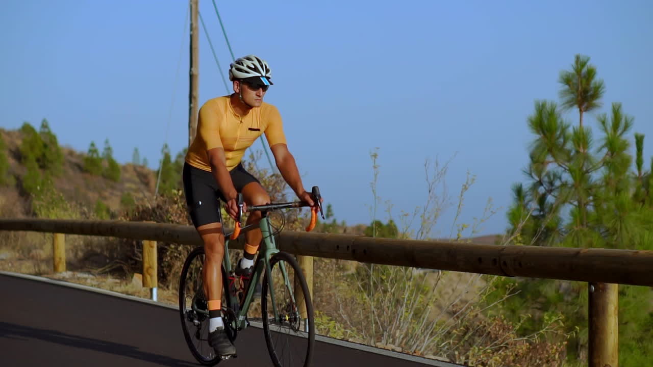 Watch as a male cyclist conquers a mountain road in this tracking video. He's dedicated to cycling training on a sunny day along a hilly highway road