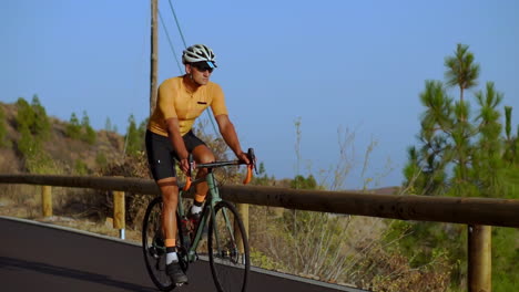 beobachten sie, wie ein männlicher radfahrer eine bergstraße in diesem tracking-video erobert. er widmet sich dem radtraining an einem sonnigen tag entlang einer hügeligen autobahn