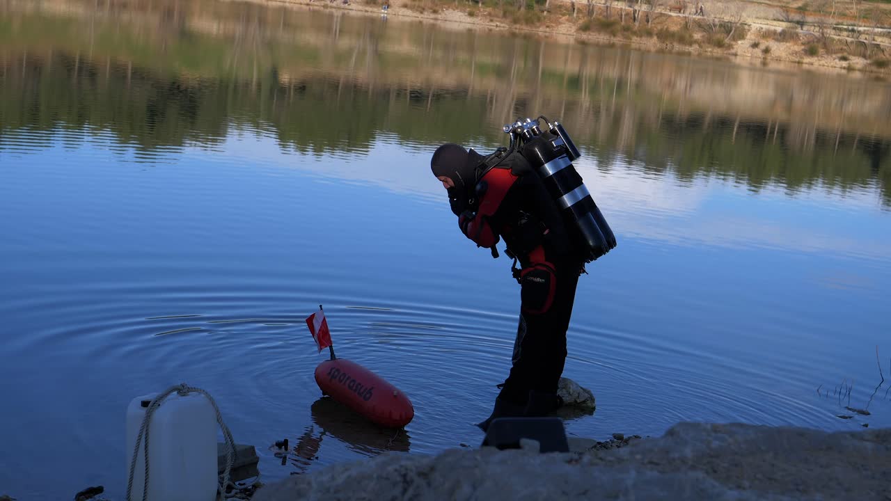 물에서 나온 잠수부가 손에 오리발을 들고 물 속으로 내려갑니다.