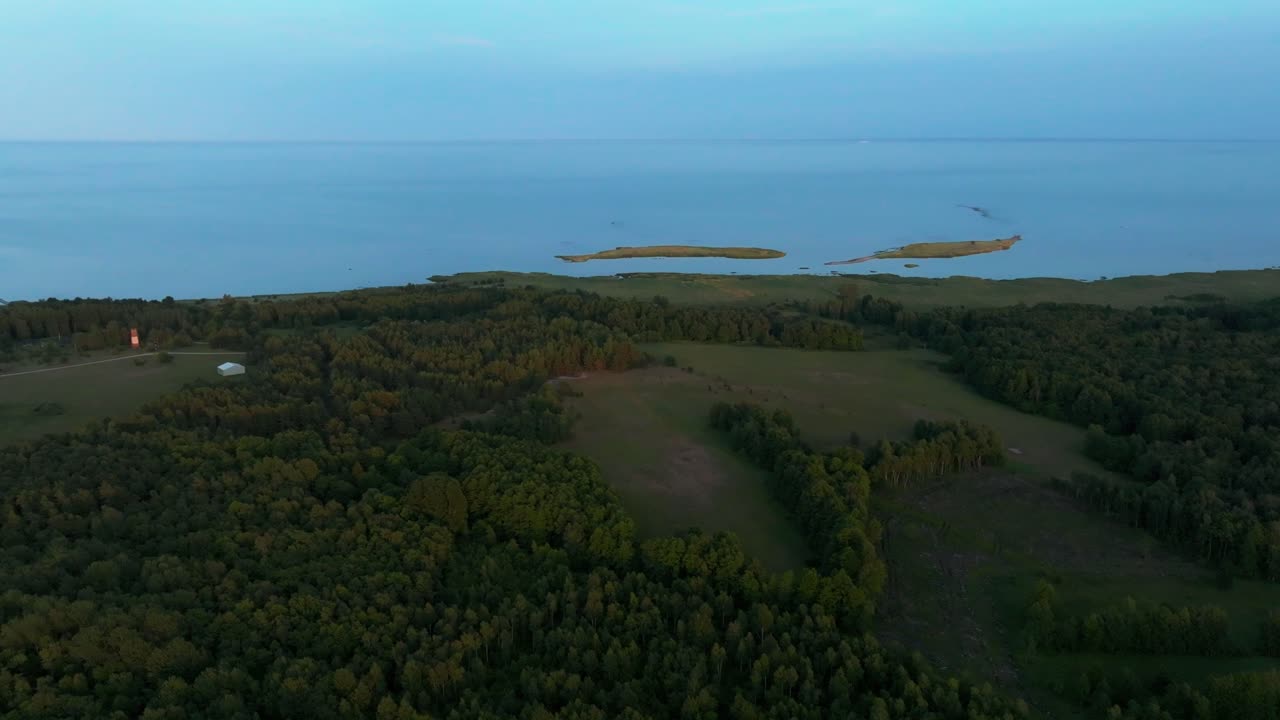 Flying over woods and fields with the coastline and sea visible in the distance. Evening light.