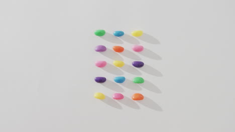 Video-of-overhead-view-of-rows-of-multi-coloured-sweets-with-copy-space-over-white-background