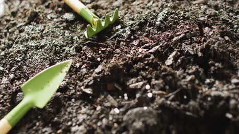 close up video of miniature trowel and rake gardening tools lying on dark soil, with copy space