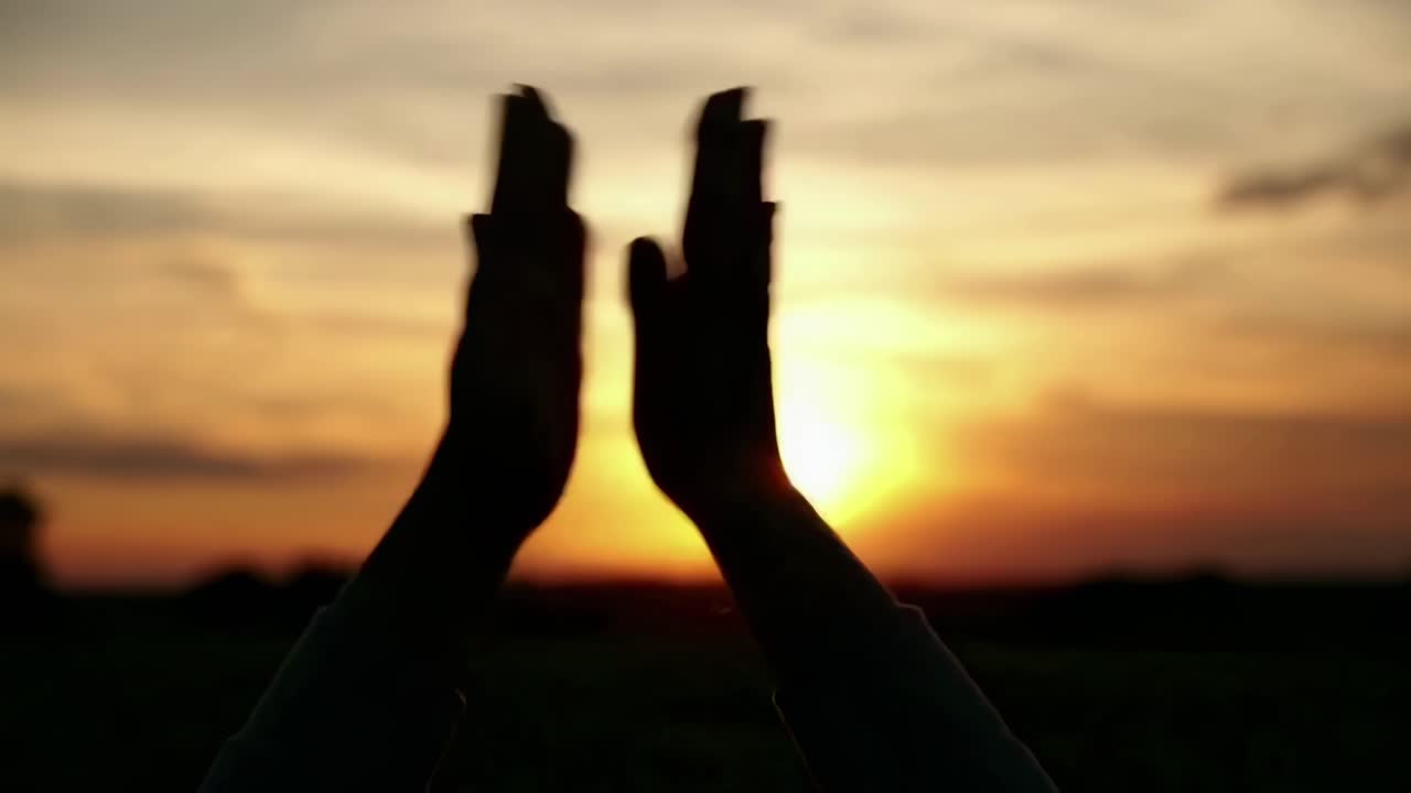 Silhuetter af hænder, der indrammer en solnedgang, filmet fra en lav vinkel, hvilket skaber et fredfyldt videoøjeblik.