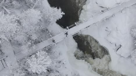 2 people walking in the snow over a bridge with waterfalls below