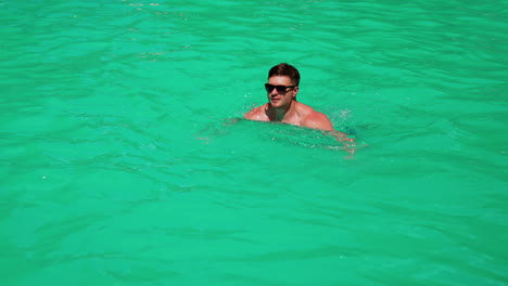 caucasian man swimming in the pool. male wearing sunglasses swims in azure water in the sun.