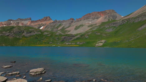 Dreamy-heavenly-Silverton-Ice-Lake-Basin-aerial-drone-cinematic-unreal-deep-sky-blue-wildflower-shoreline-Silverton-Colorado-lush-green-summer-incredible-snow-melting-Rocky-Mountains-forward-reveal
