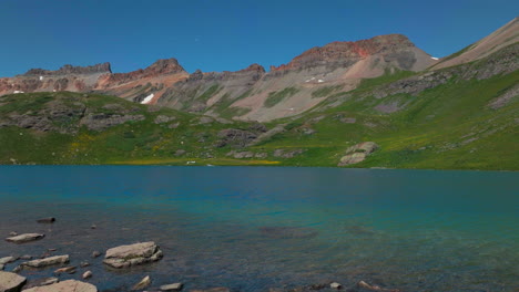 dreamy heavenly silverton ice lake basin aerial drone cinematic unreal deep sky blue wildflower shoreline silverton colorado lush green summer incredible snow melting rocky mountains forward reveal