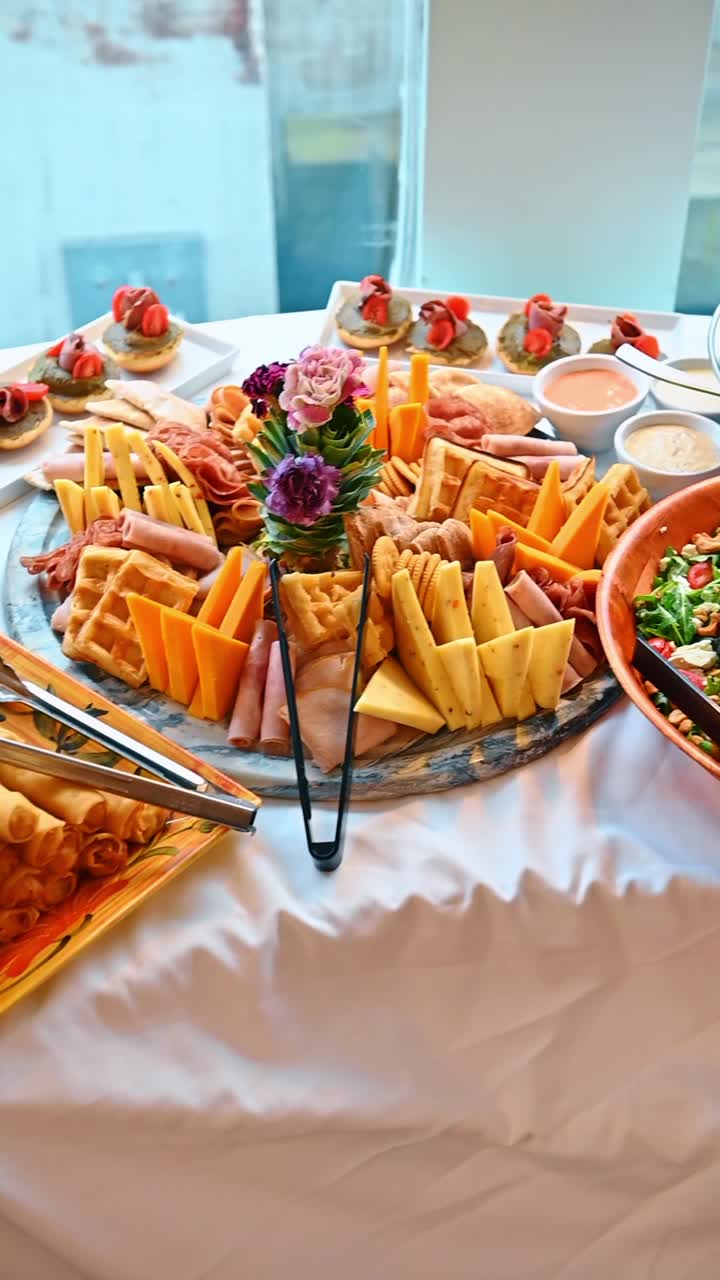 Roast beef affettato e bastoncini di mozzarella su tavolo da catering. Ciotola di vetro con insalata greca, affettati e bastoncini di mozzarella impanati in un vassoio di legno a barca.