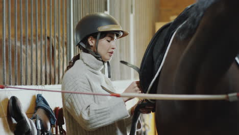 woman fastening straps while saddling horse