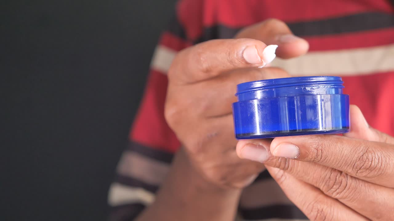 hombre aplicando crema de un frasco azul