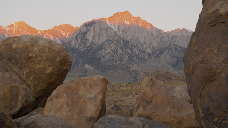 sunrise on slightly snowy mount whitney with alabama hills and boulders in foreground