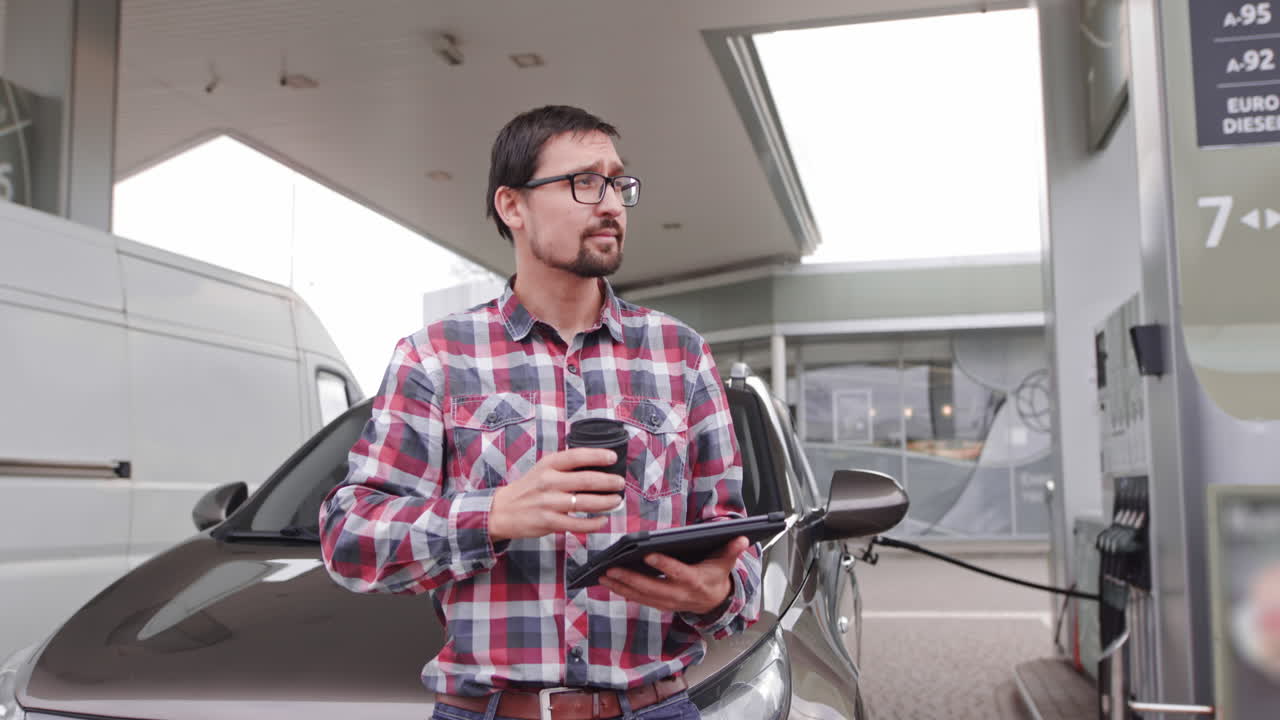 Man at gas station using tablet and drinking coffee