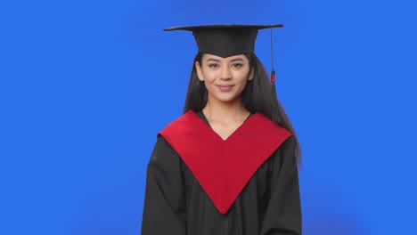 retrato de una estudiante en traje de graduación de gorra y túnica quita la máscara médica protectora. joven mujer morena posando en el estudio con fondo de pantalla azul. primer plano. cámara lenta lista 59.94fps