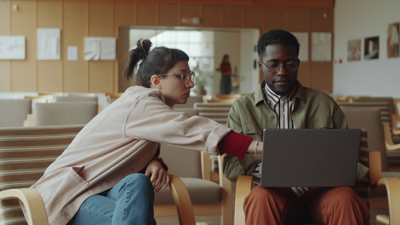 colegas multiétnicos trabajando en una computadora portátil en el auditorio de la biblioteca