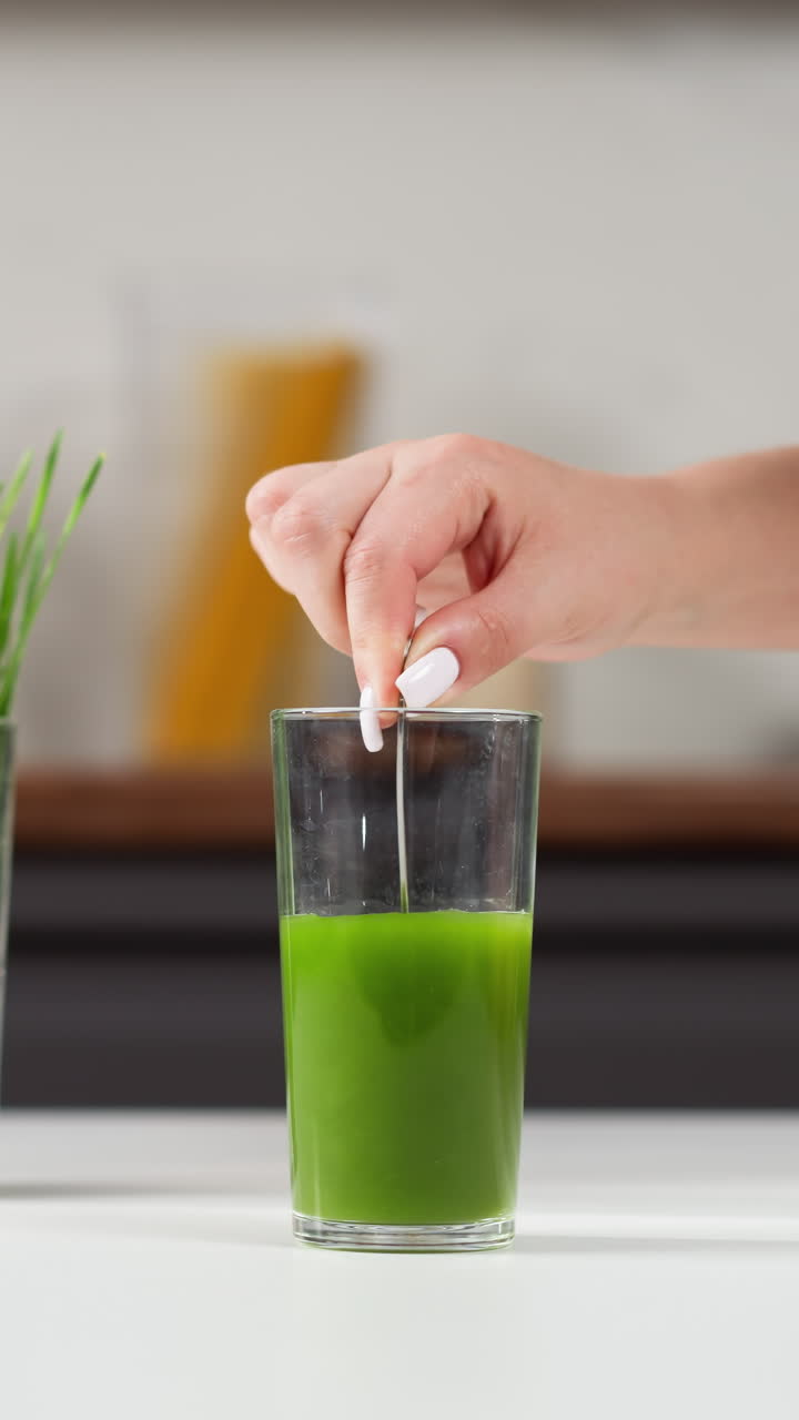 손으로 녹색 주스 한 잔에 을 넣고, 배경에는 밀 풀이 있습니다.