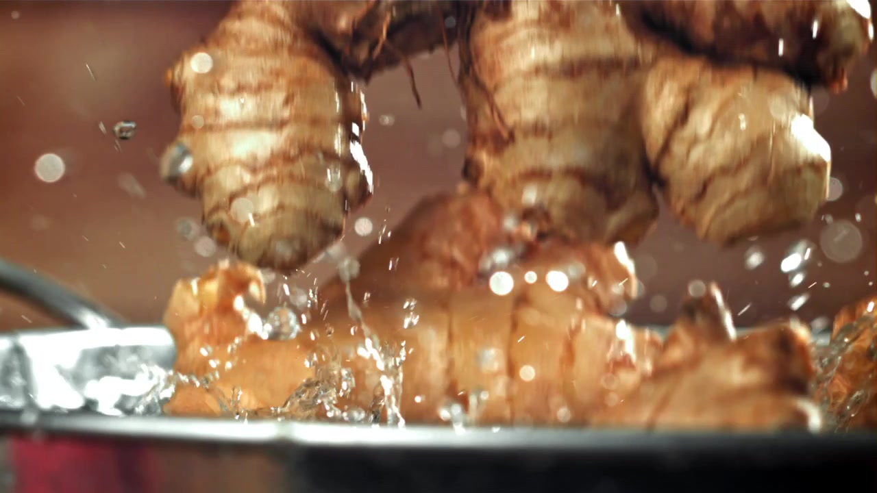 Tuoreet inkiväärinjuuret roiskuvat veteen hidastettuna.