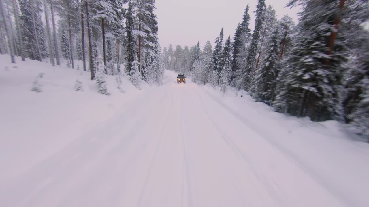 Drone flying towards a 4x4 car driving in a cross country road covered in snow during mid winter solstice