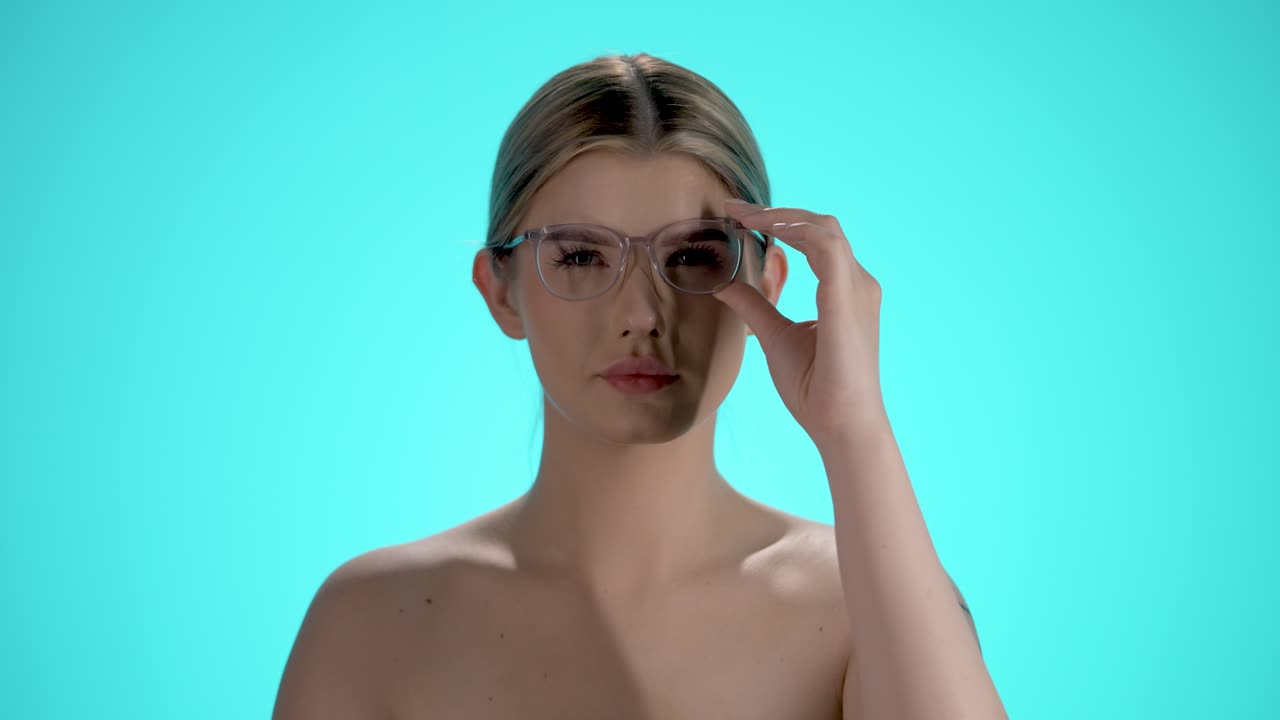 Medium shot of a pretty young woman wearing glasses who has put on her glasses to have better eyesight and see better in front of turquoise background in slow motion