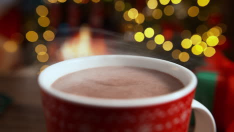 steaming mug of hot cocoa by the fireplace decorated with a garland of christmas lights