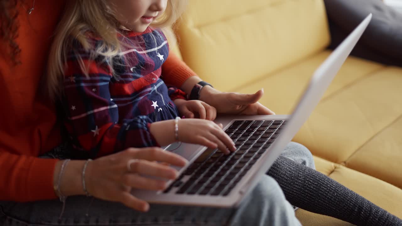 Mother and daughter sitting on the couch, typing on laptop keyboard
