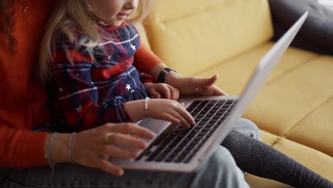 Mother-and-daughter-sitting-on-the-couch,-typing-on-laptop-keyboard