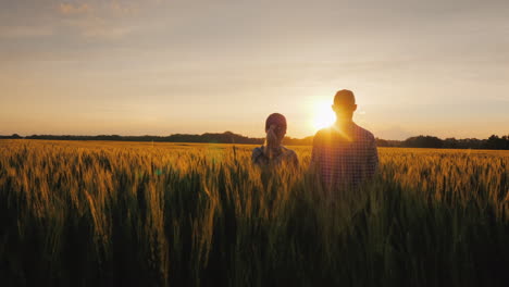 dos granjeros, un hombre y una mujer, esperan la puesta de sol sobre un campo de trabajo en equipo de trigo en ag