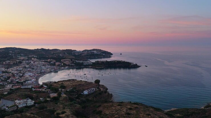 Vista aerea con drone di una baia turistica con una città collinare e un promontorio roccioso, Agia Pelagia, Grecia