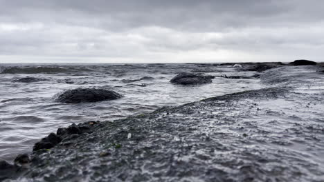 shot looking across a rock pool with the water slashing up over the rocks, on a grey and cloudy day