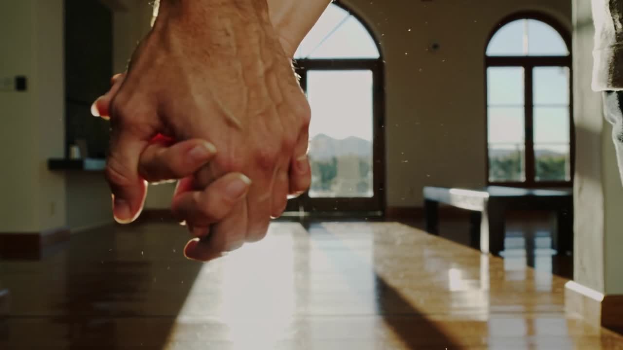 Entering frame, two adult hands descending and locking fingers in sunlit hall, bare arms bonding