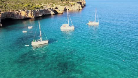 sailboats gently float in the turquoise waters of cala varques, nestled near porto cristo in majorca. this beautiful cove features stunning cliffs and serene surroundings, perfect for relaxation.