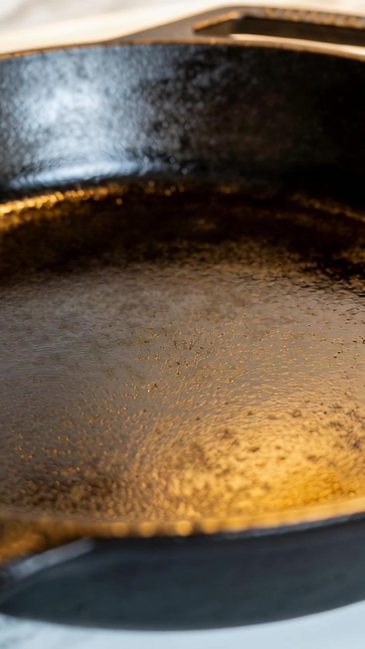Vertical video: Shifting camera revealing seasoned cast iron skillet on stovetop, warm reflections