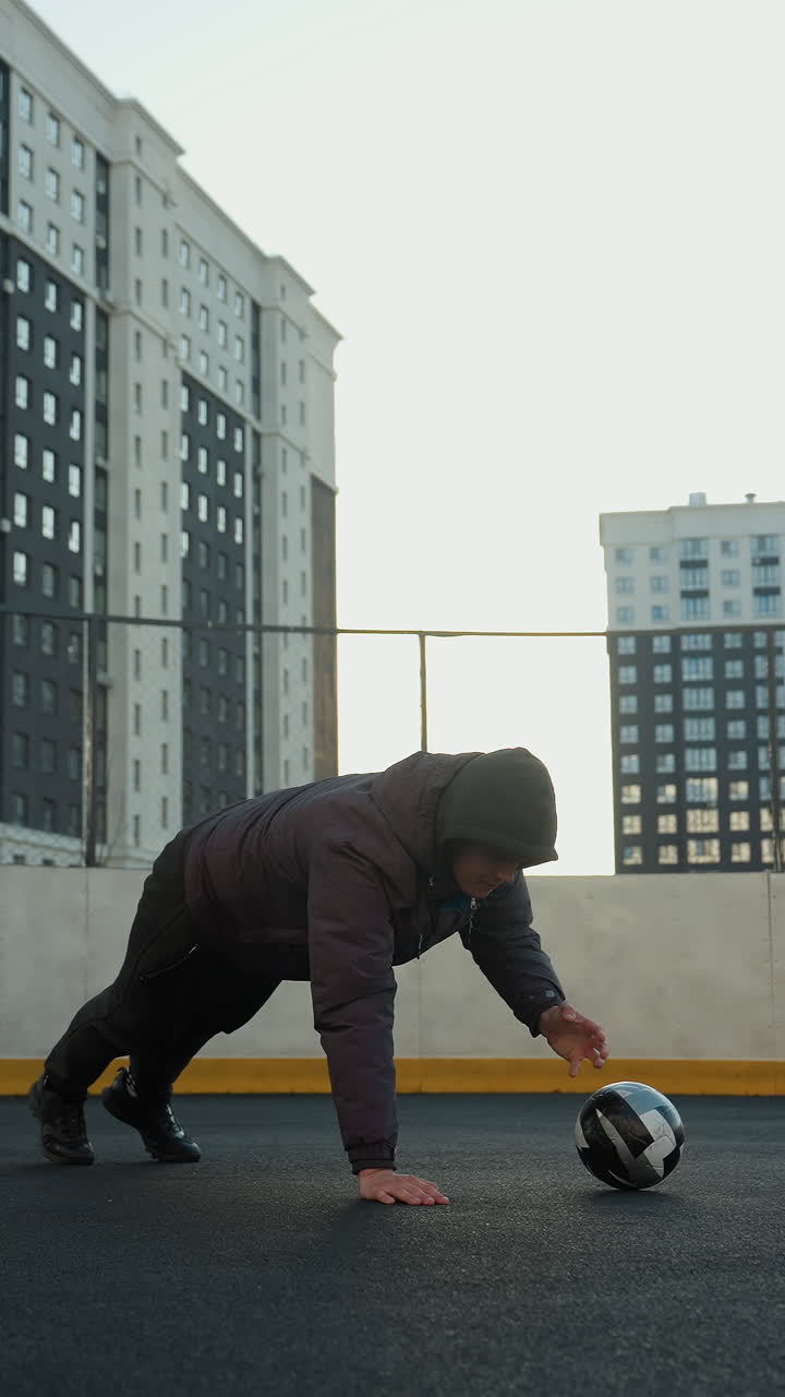 Athlete performing dynamic push-ups alternating hand placement on a soccer ball demonstrating strength, coordination, and agility against a backdrop of goal post and residential buildings