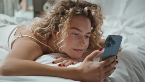 restful woman using mobile phone lying in bed closeup. serene girl scrolling