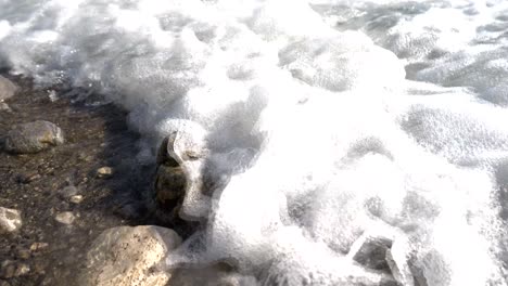 Beach-in-Greece,-foamy-waves-of-the-Ionian-Sea-washing-over-stones-on-the-shore