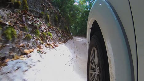 Vista-De-Punto-De-Vista-Más-Allá-De-La-Rueda-Delantera-De-Un-Camión-Todoterreno-Blanco-4wd-Desde-Una-Cámara-Montada-En-Un-Automóvil,-Mientras-Rebota-A-Lo-Largo-De-Un-Sendero-Interior-Arenoso-A-Través-De-La-Selva-Tropical-Con-Empinados-Terraplenes-Arenosos