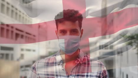 Animation-Der-Flagge-Englands-über-Einem-Lateinamerikanischen-Mann-Mit-Gesichtsmaske-In-Der-Stadtstraße
