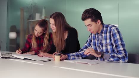 Gruppe-Junger-Leute-Beim-Treffen-In-Einer-Modernen-Wohnung.-Drei-Schüler-Arbeiten-An-Ihren-Hausaufgaben,-Sitzen-Zusammen-Am-Tisch-Und-Trinken-Kaffee.-Zeitlupenaufnahme