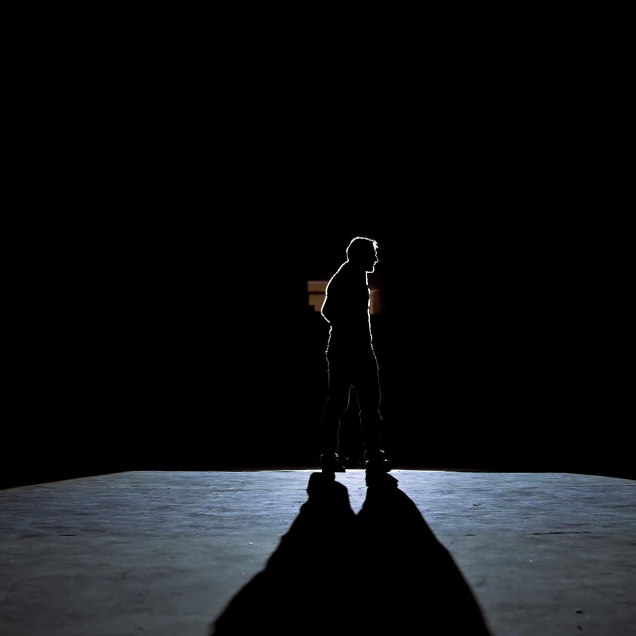 Actor man on a stage. Dark silhouette of a man wearing suit performing on a scene in theatre at spotlight. View from the stage