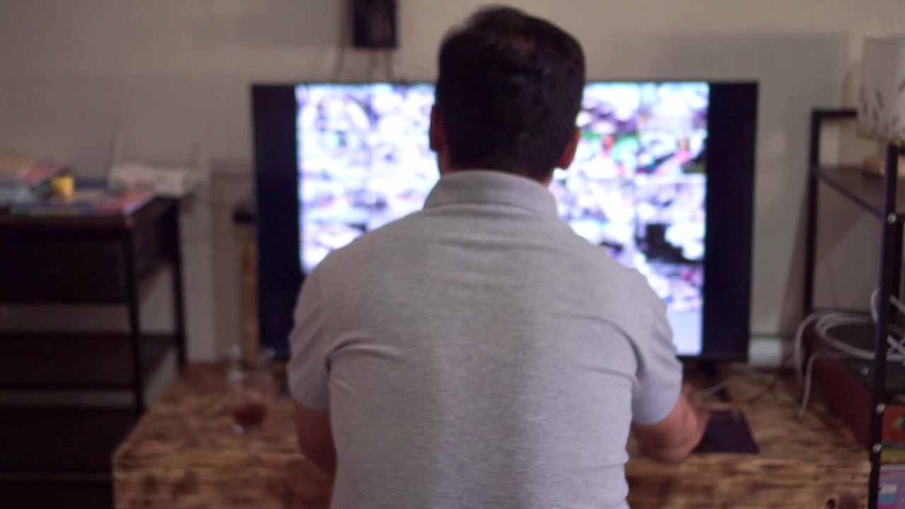Vista posteriore di un uomo che guarda i feed in diretta delle telecamere di sicurezza su due schermi, sala di controllo buia, concetto di monitoraggio CCTV e osservazione del sistema di sorveglianza